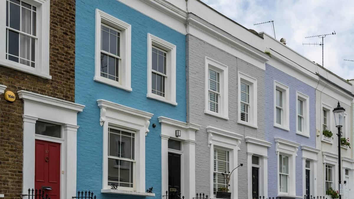 A row of painted terraced houses in blue, grey and lilac with black railings and white window frames on a Notting Hill street