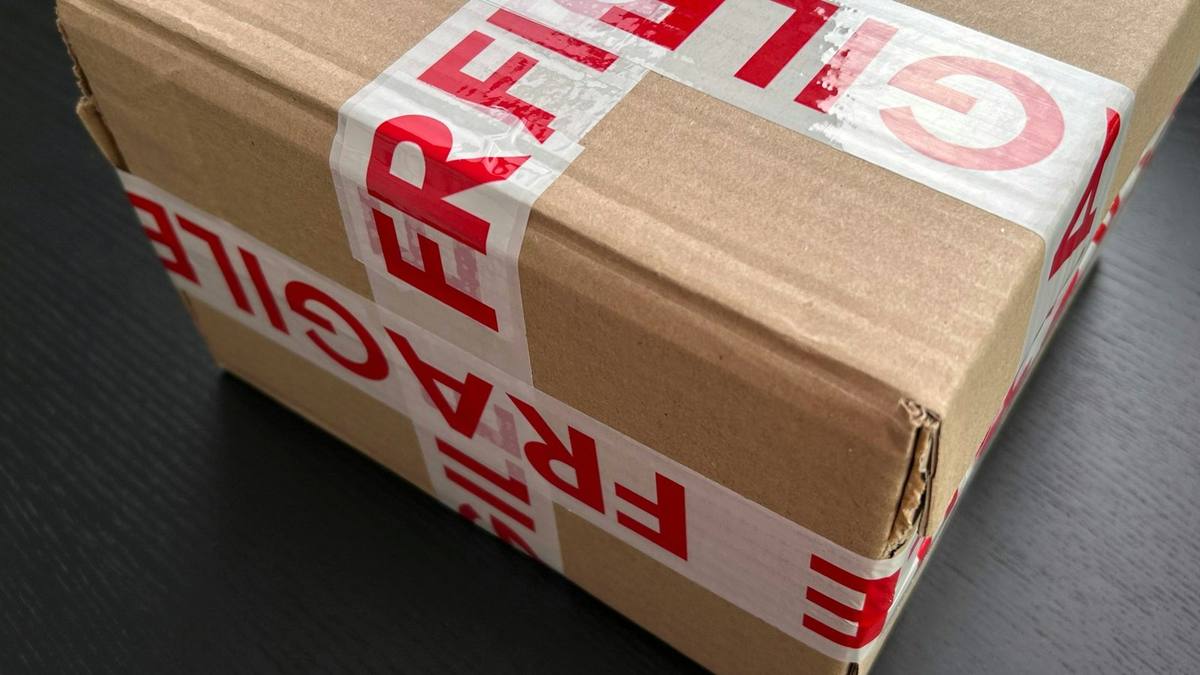 Cardboard parcel sealed with red and white fragile tape on a dark table