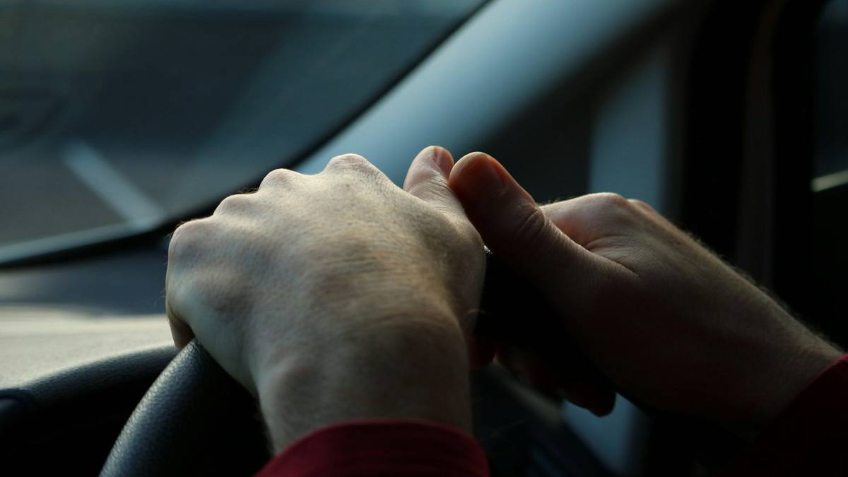 Close-up of two hands on a car steering wheel, with the windscreen and side window softly out of focus