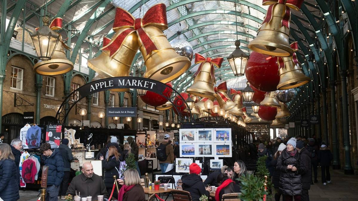 Shoppers browse craft and art print stalls beneath giant red bows and gold bells in the Apple Market at Covent Garden