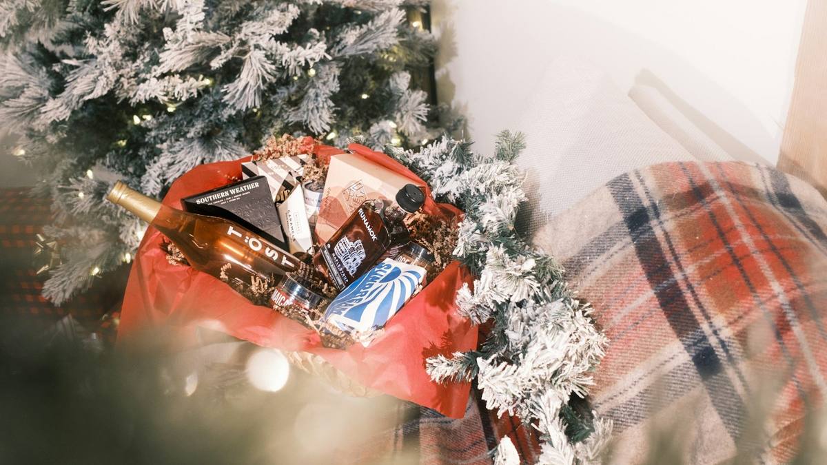 A wicker hamper of Christmas food and drink, lined with red tissue, under a snowy tree