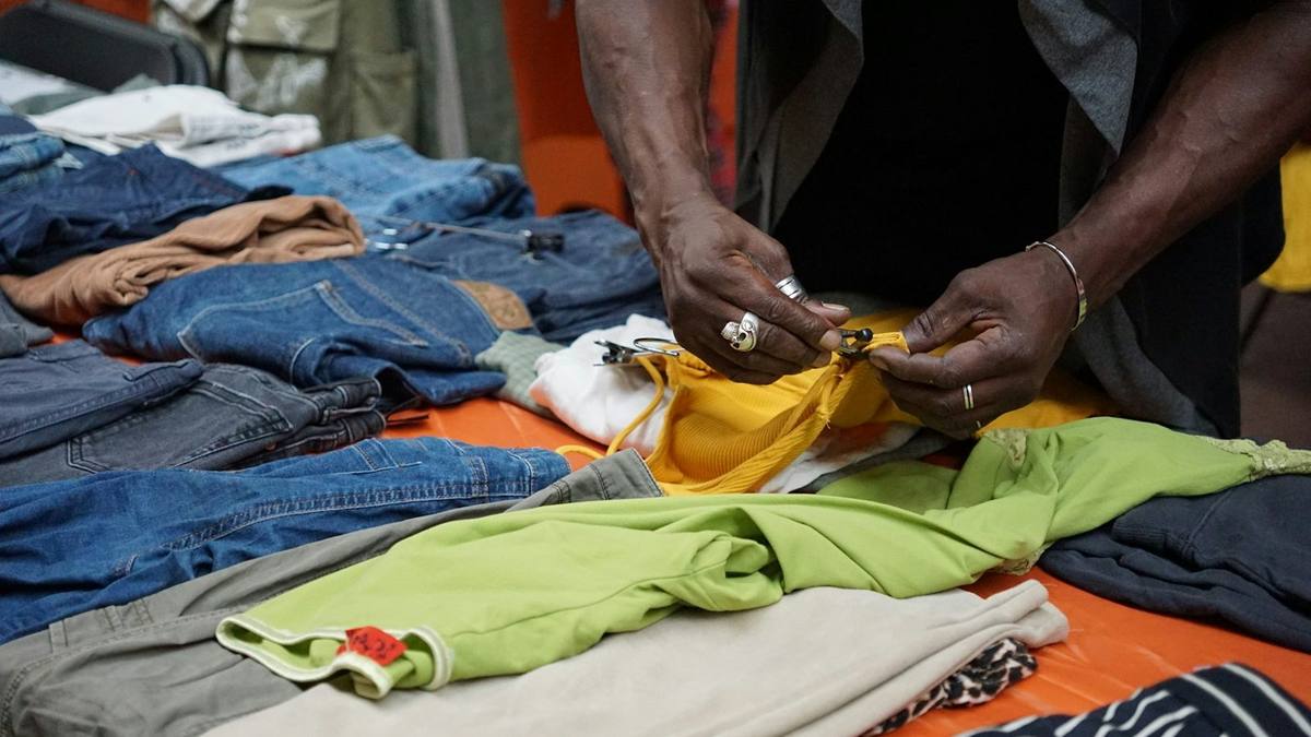 Hands sorting folded second-hand jeans and tops on a table, with a small red tag on one of the tops