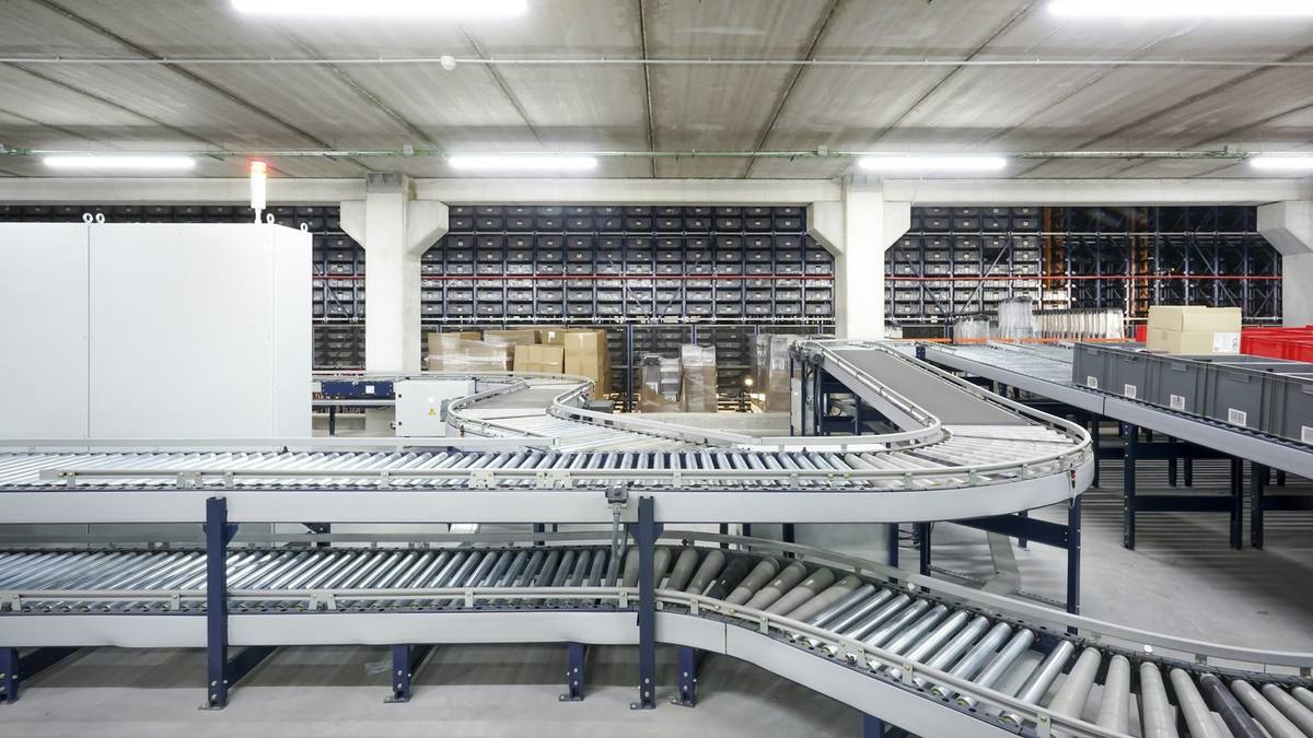Roller conveyors curving through a large warehouse, with storage racks behind