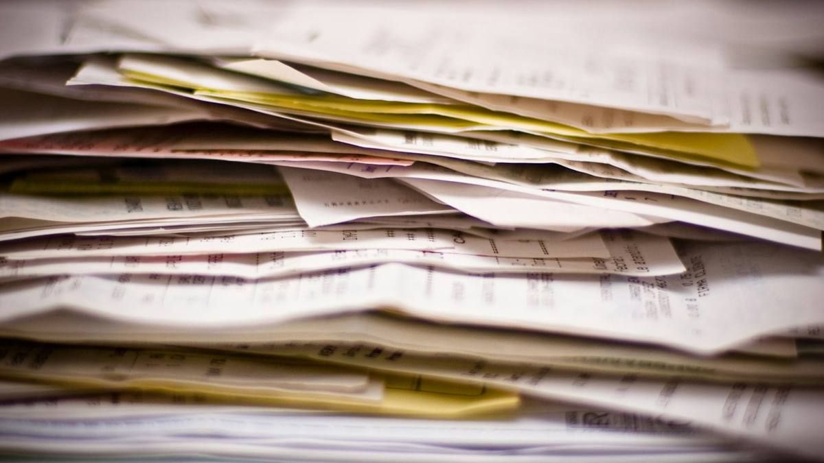 A tall, untidy stack of paper invoices, receipts and folders, seen side on