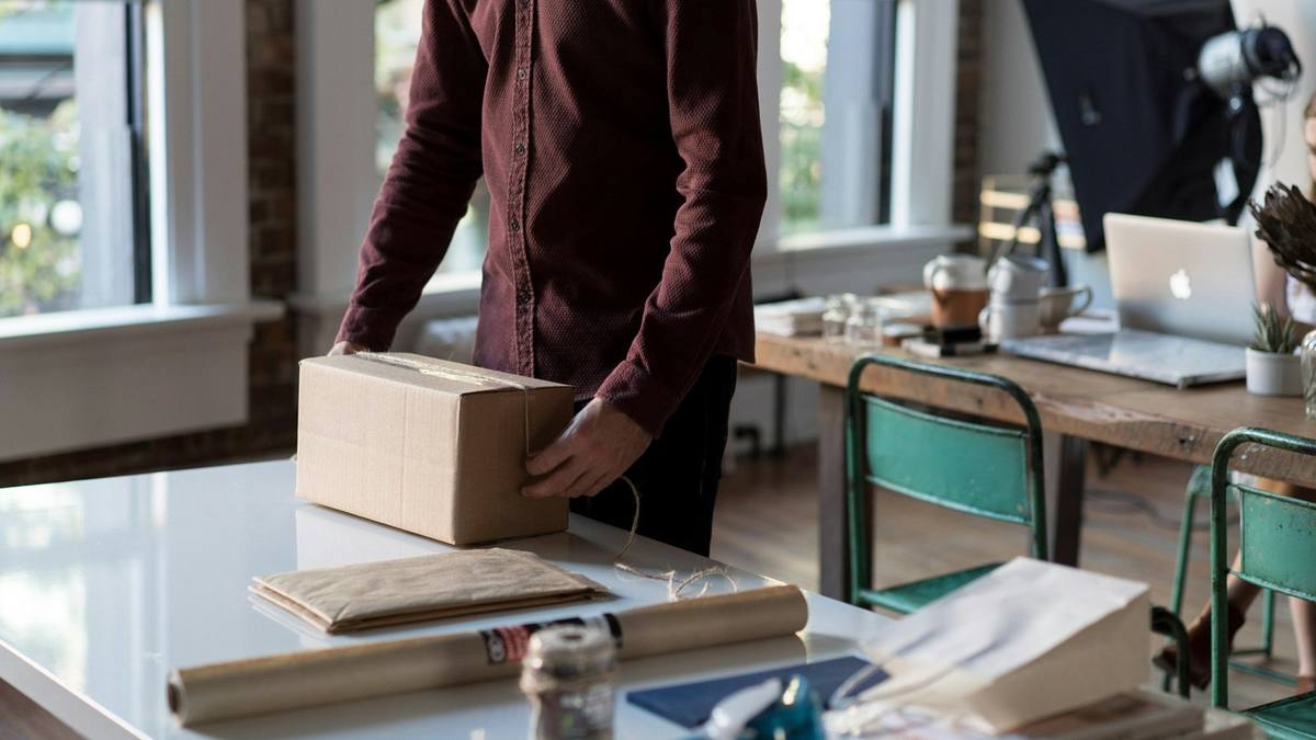 A person packing a cardboard box at a desk