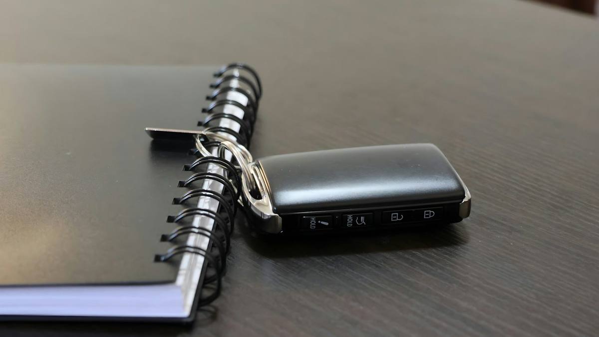 A car key fob resting on a black ring-bound notebook on a dark wooden desk