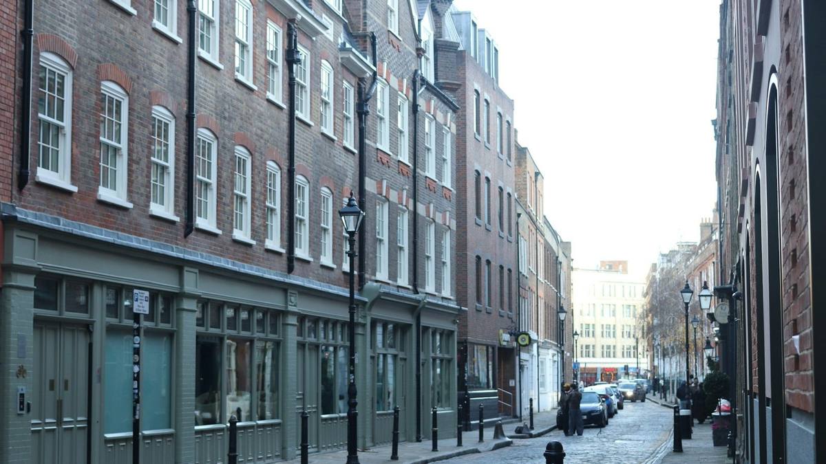 A quiet cobbled street of brick buildings with shopfronts at ground level and old street lamps