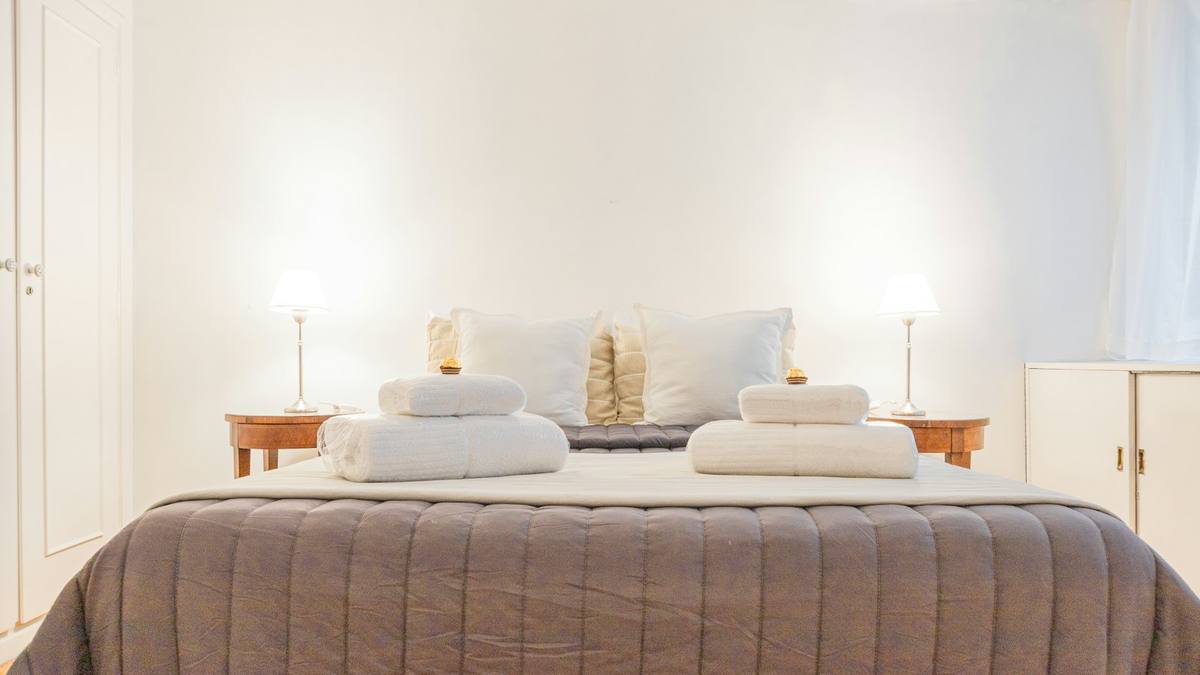 A neatly made bed with folded white towels in a bright bedroom