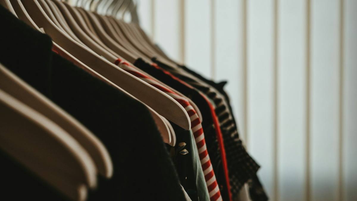 Shirts and jackets hanging on wooden hangers on a clothes rail, seen close up from one end
