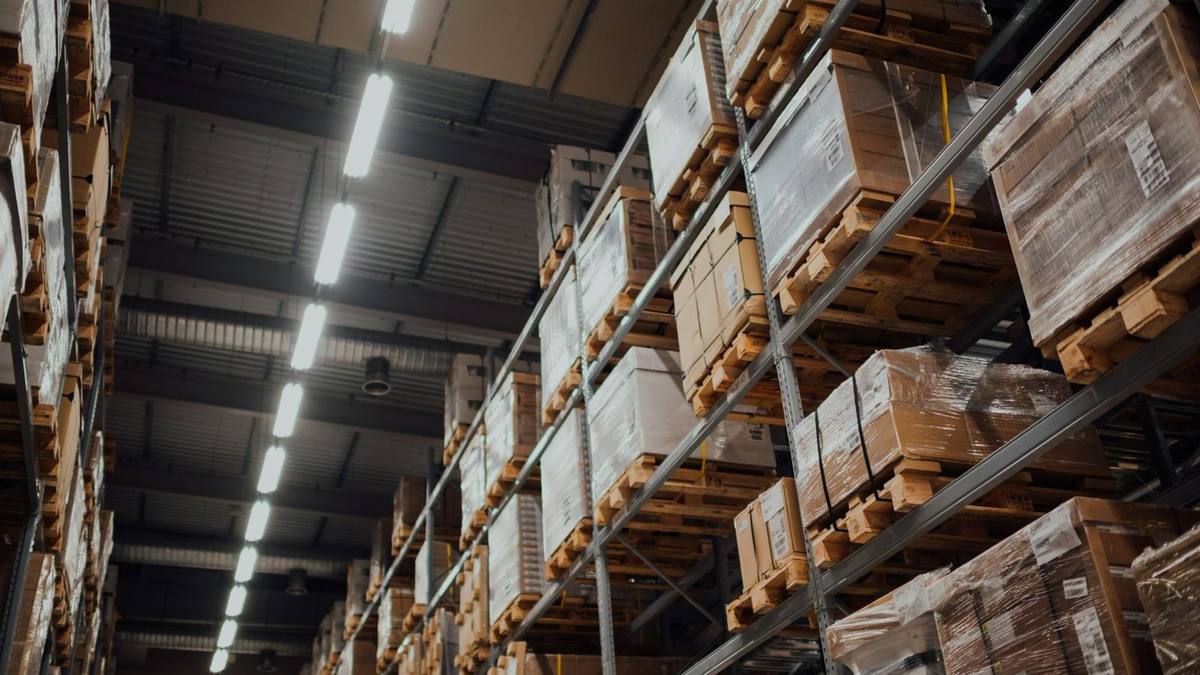 Tall warehouse racking stacked with cardboard boxes and shrink-wrapped pallets under strip lights
