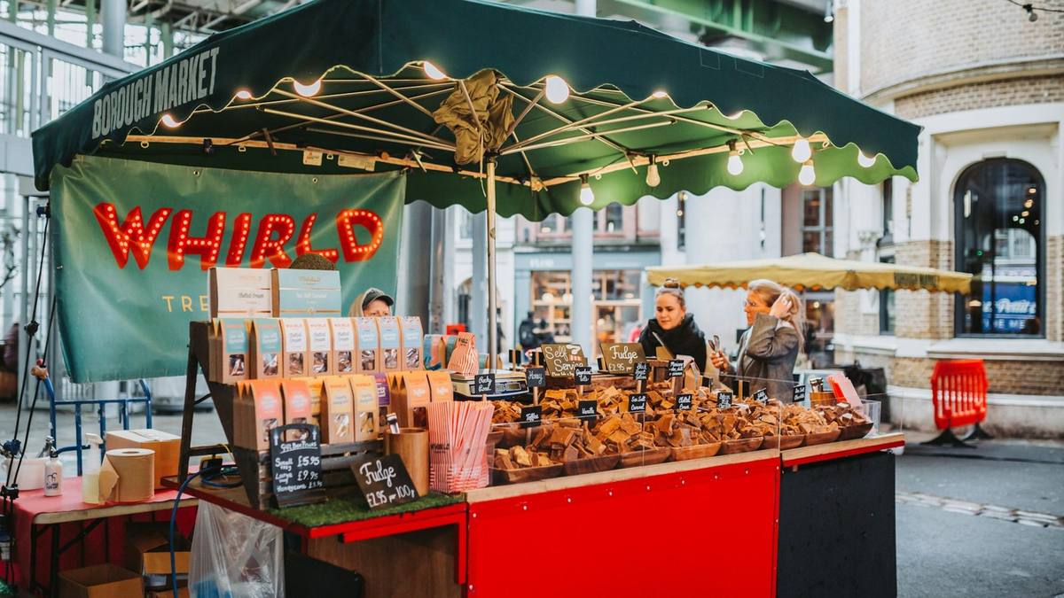 A trader behind a red food stall under a green awning at Borough Market in London