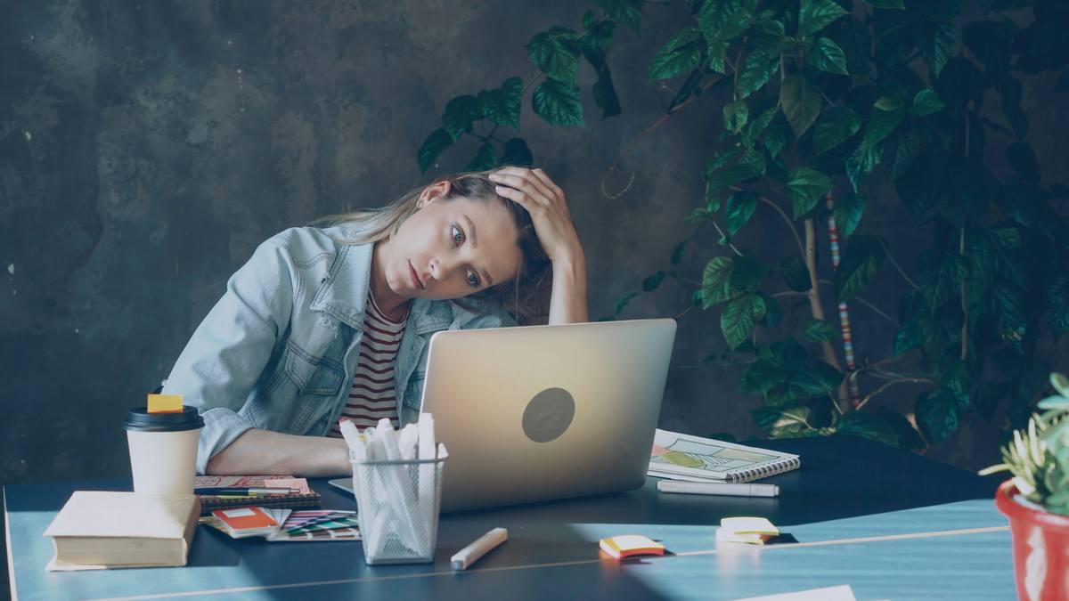A female student looking at a laptop and pulling a stressed expression.