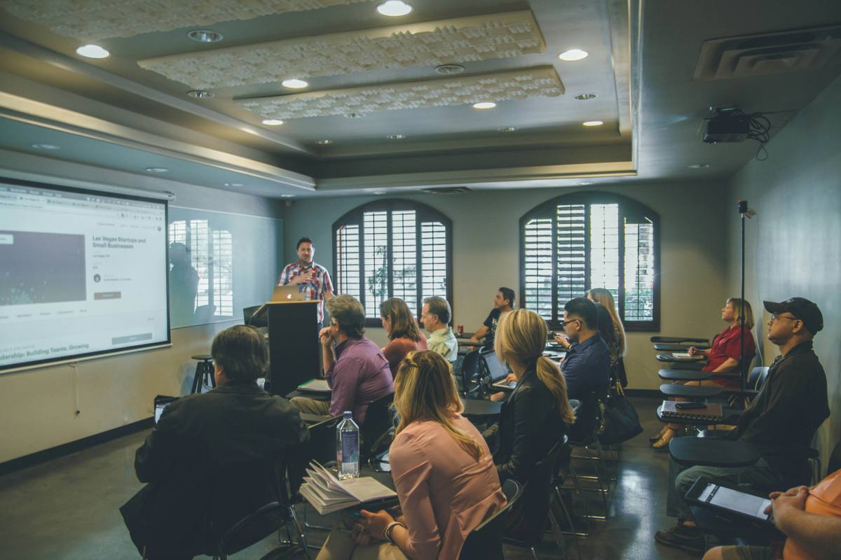 Students attending a university lecture in a classroom while a speaker presents at the front.