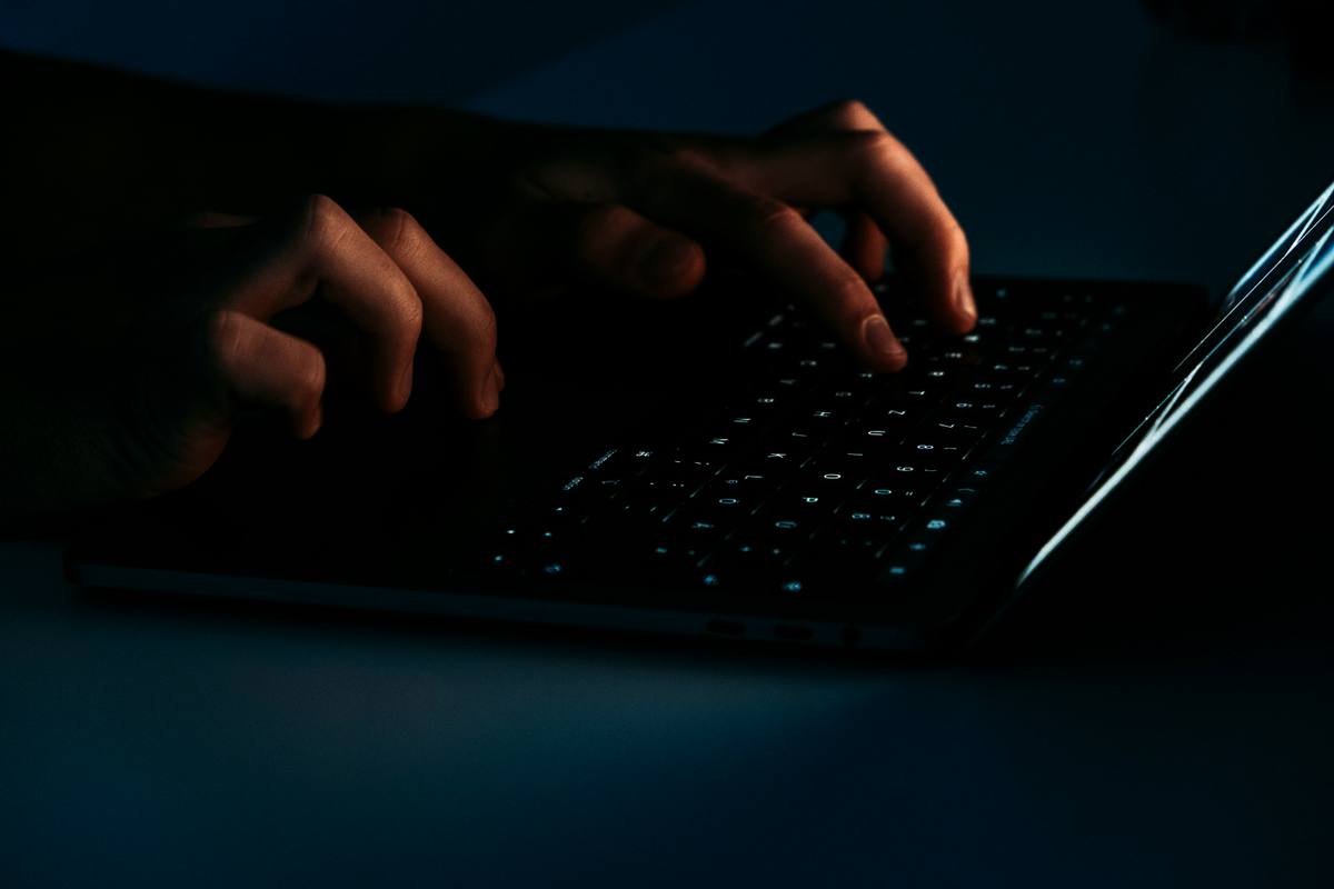 Person using a black laptop computer in a dark room.