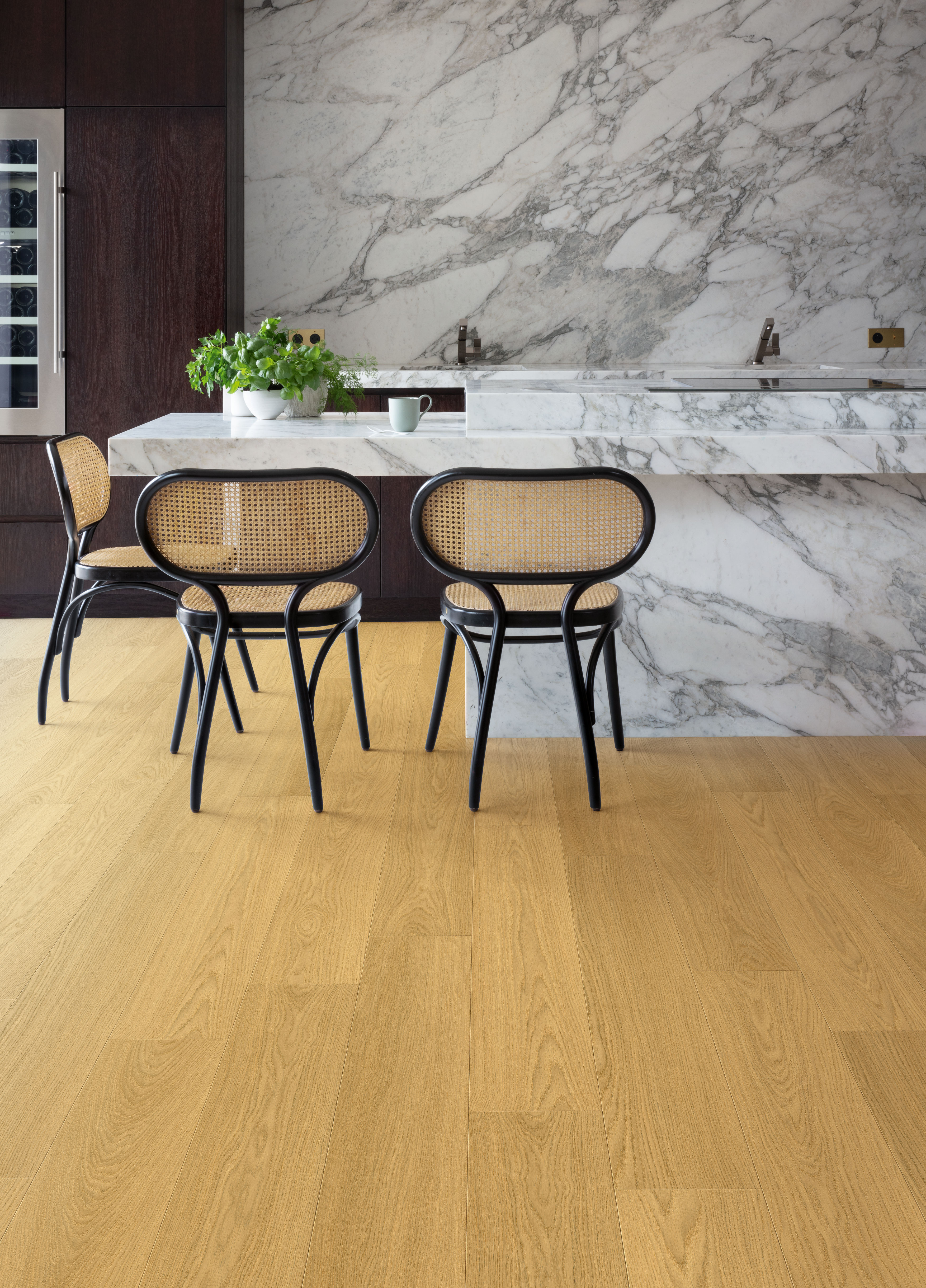 Modern kitchen with marble surfaces, dark cabinetry, cane chairs and warm natural oak flooring.