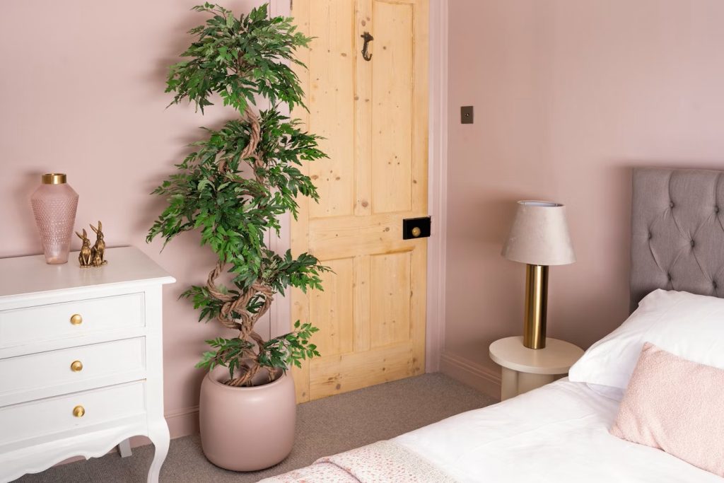 Bedroom with soft pink walls, and a large potted plant that provides some lush greenery